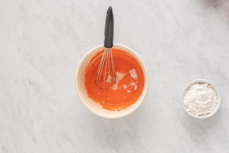 whisking egg yolks, sugar, and strawberry jello in a white bowl.