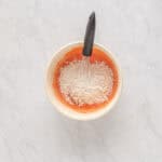 adding flour to jello-and-egg mixture in a white bowl with a whisk.