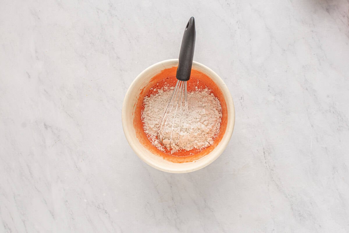 adding flour to jello-and-egg mixture in a white bowl with a whisk.