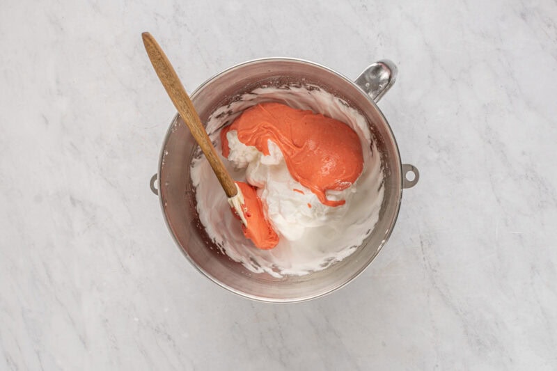 folding strawberry egg yolk mixture into egg white meringue in a mixing bowl with a rubber spatula.
