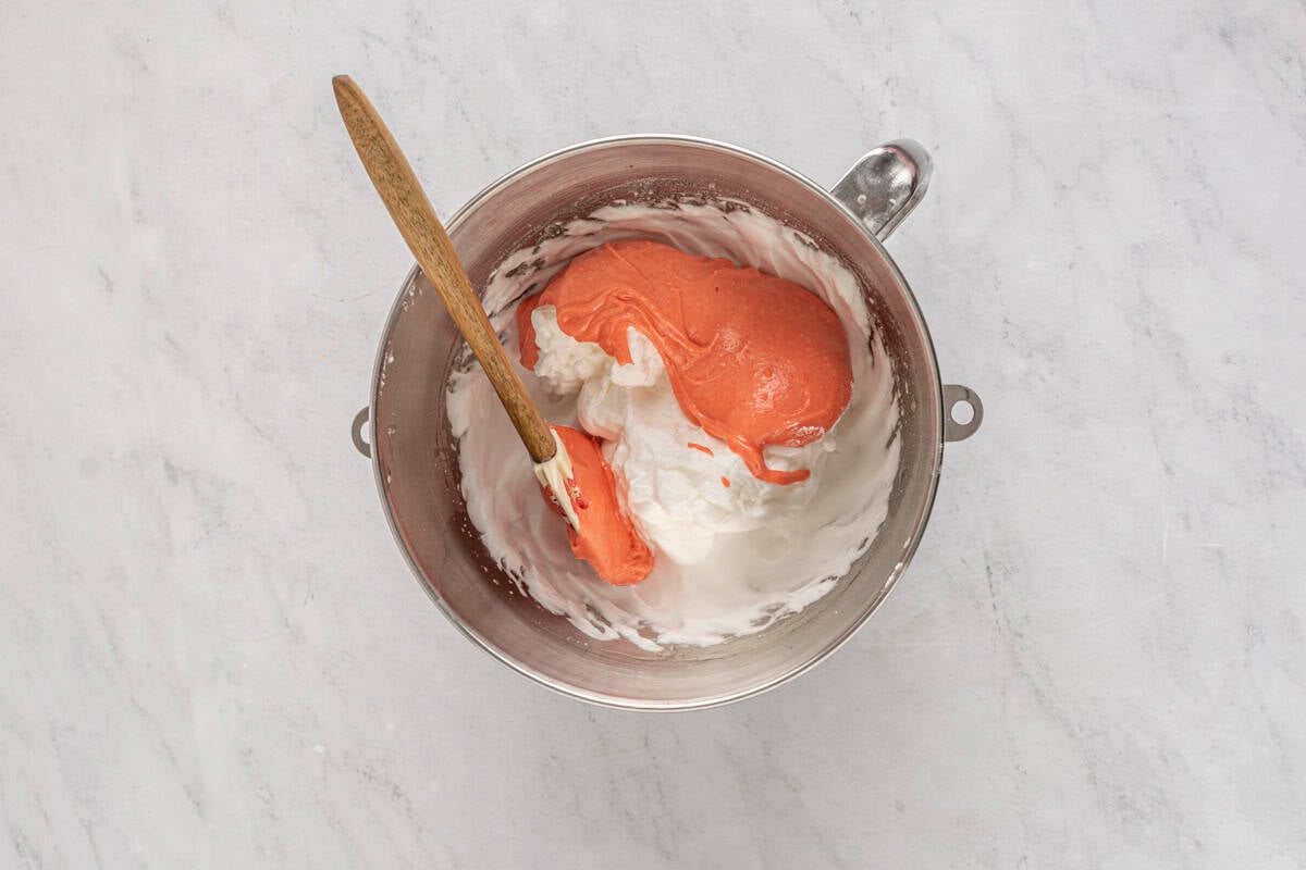 folding strawberry egg yolk mixture into egg white meringue in a mixing bowl with a rubber spatula.