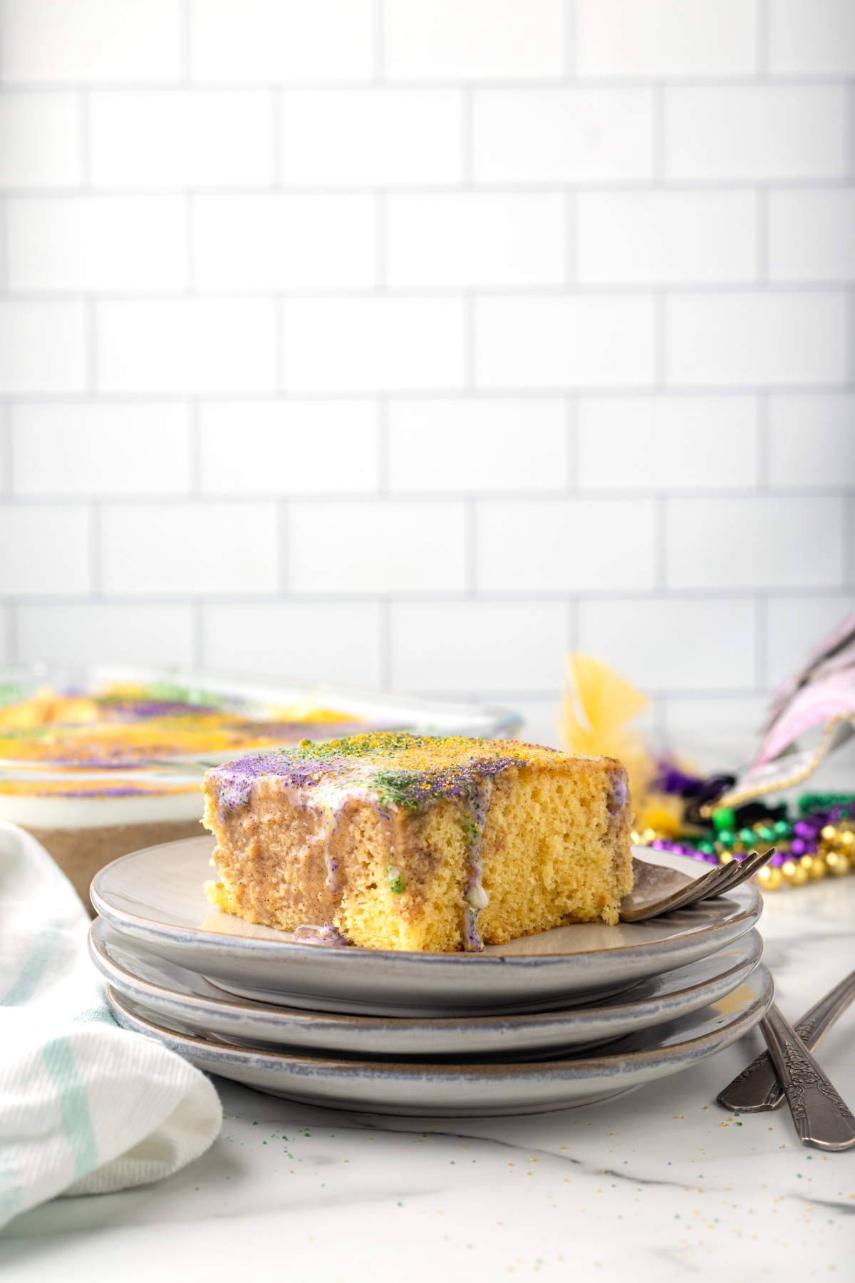 side view of a slice of king cake poke cake on a stack of white plates.