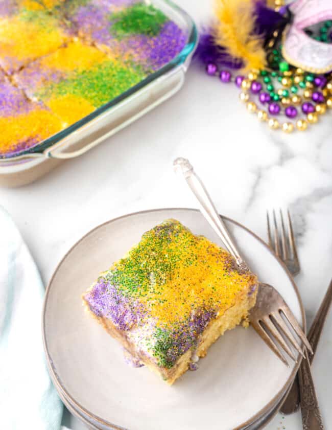 a slice of king cake poke cake on a white plate with a fork.