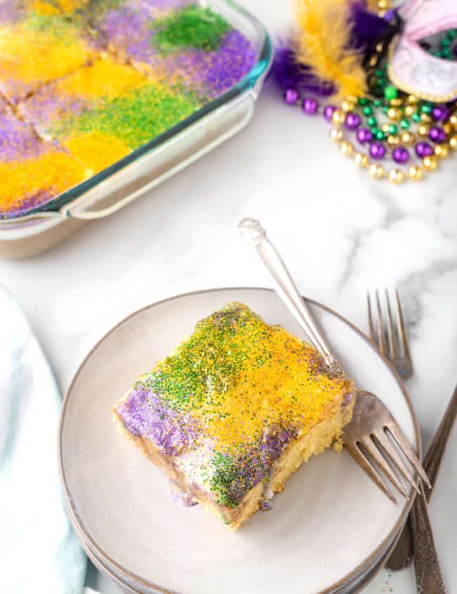 a slice of king cake poke cake on a white plate with a fork.