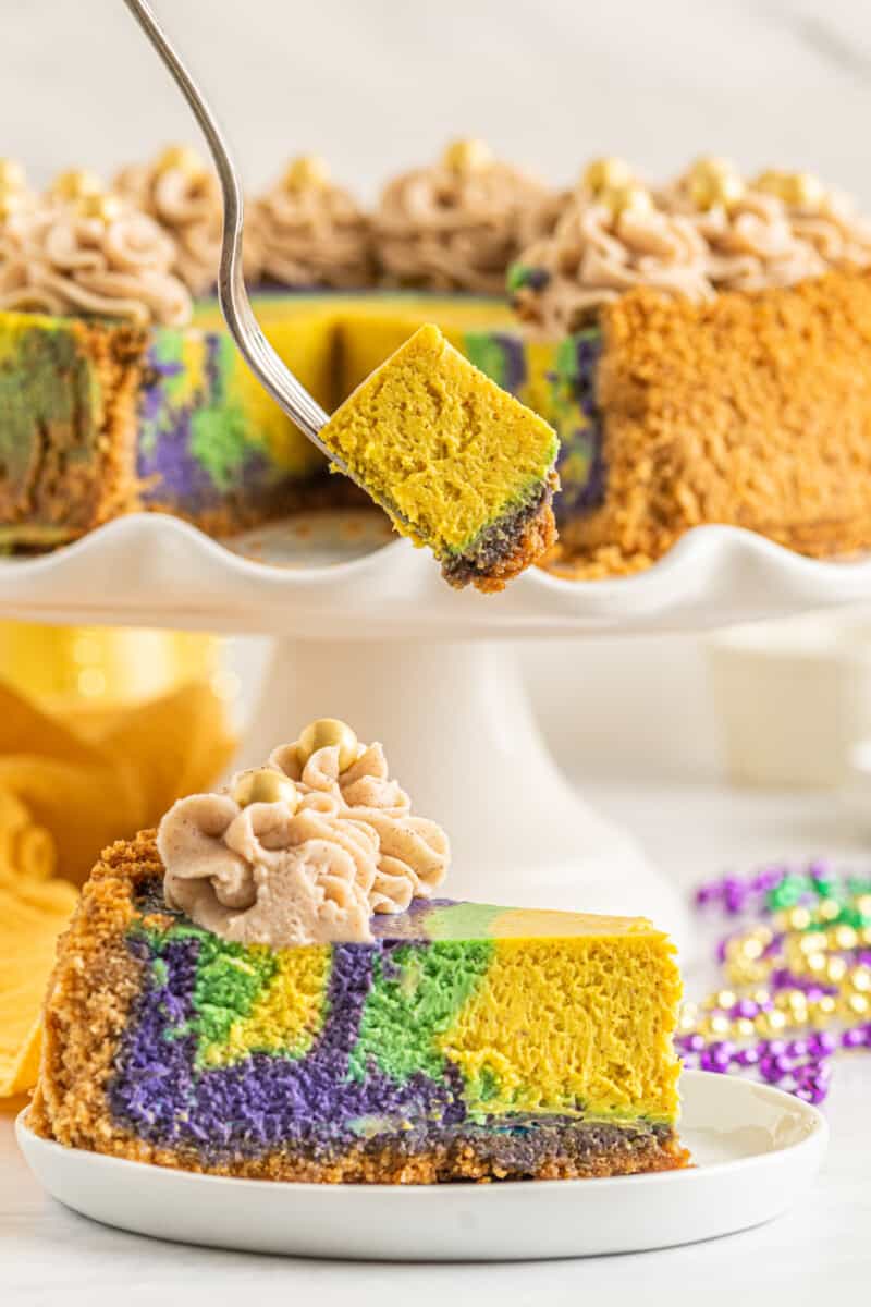a forkful of king cake cheesecake hovering above a slice of king cake cheesecake on a white plate.