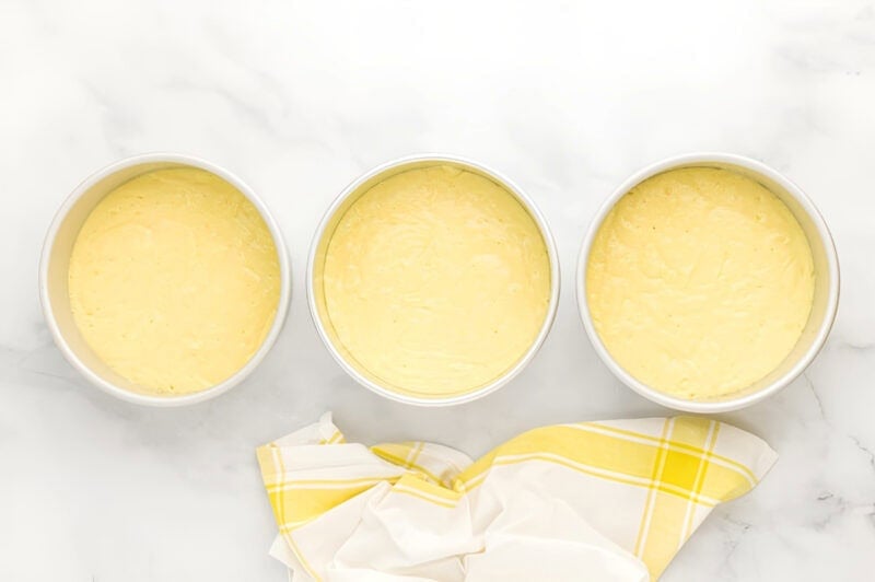 lemon cake batter divided between three round cake pans.