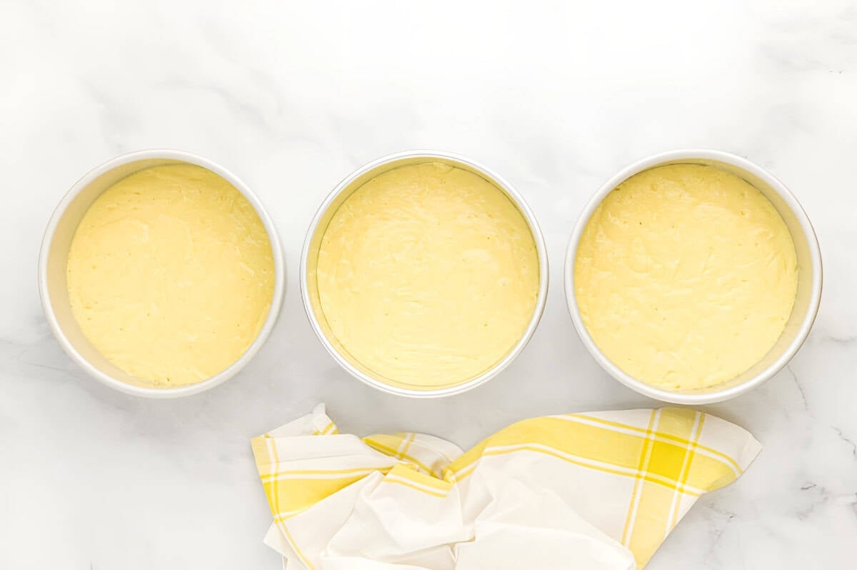 lemon cake batter divided between three round cake pans.
