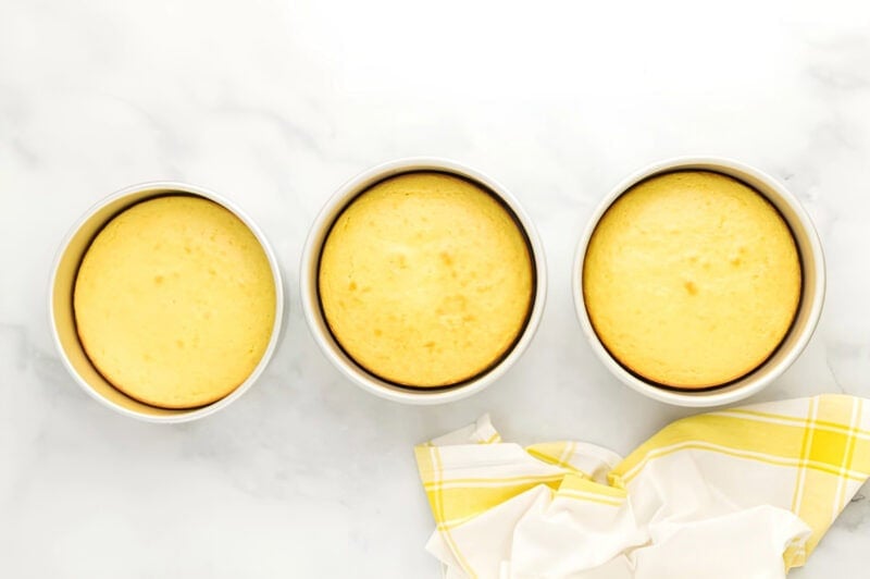 three baked lemon cake layers in round cake pans.