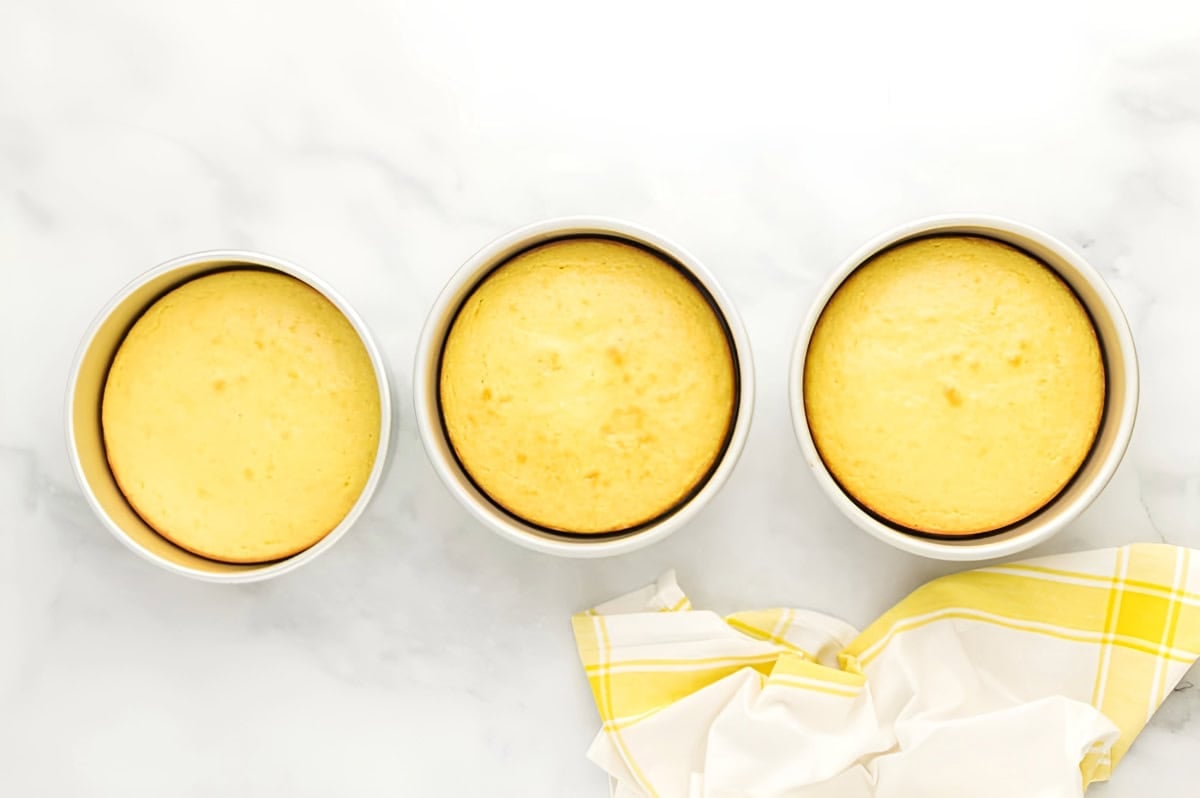 three baked lemon cake layers in round cake pans.
