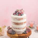 side view of naked cake on a wooden cake board topped with berries.