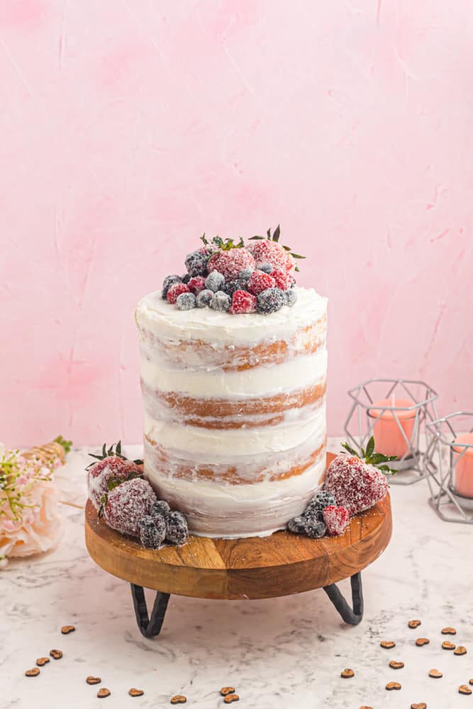 side view of naked cake on a wooden cake board topped with berries.