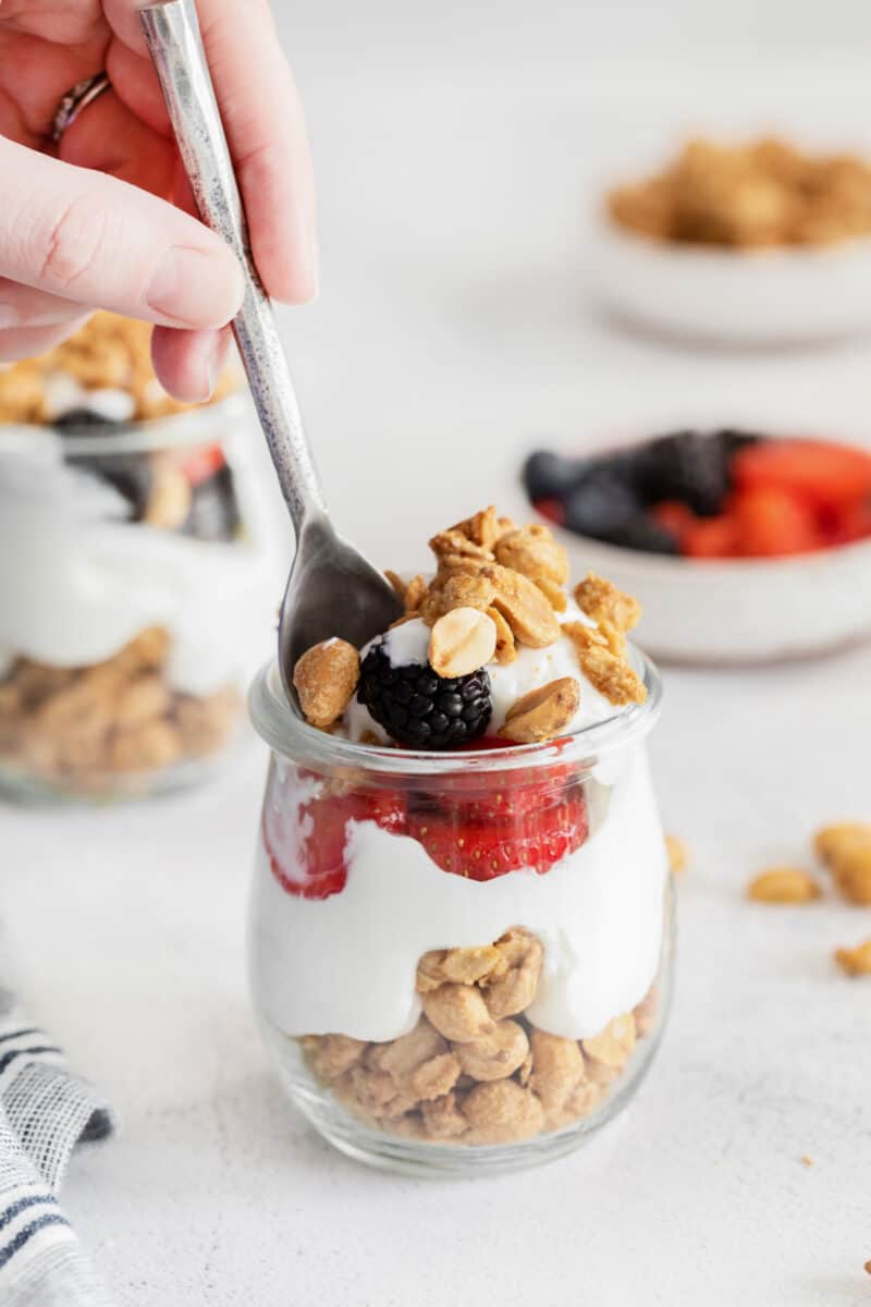 side view of a hand using a spoon to scoop pb&j granola parfait from a glass jar.