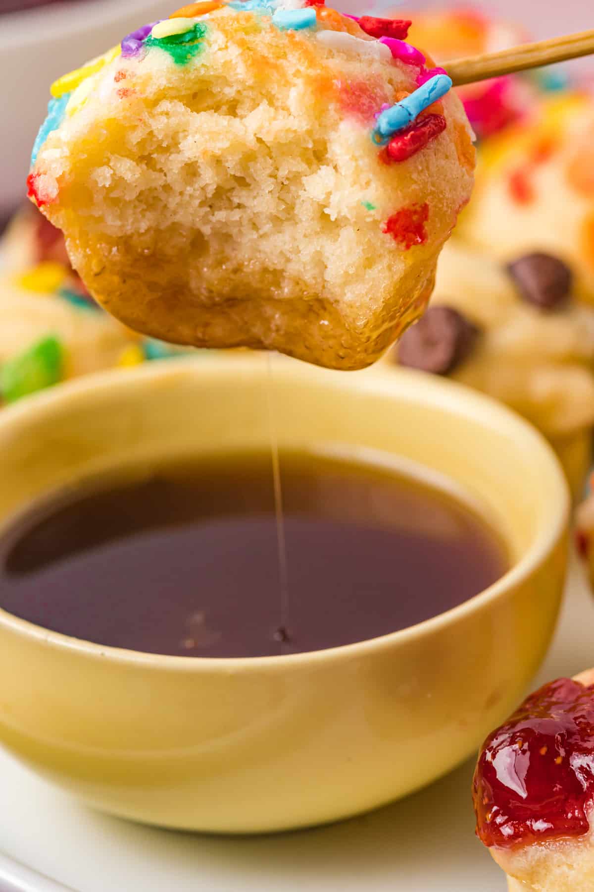 dipping a mini pancake muffin into a bowl of syrup