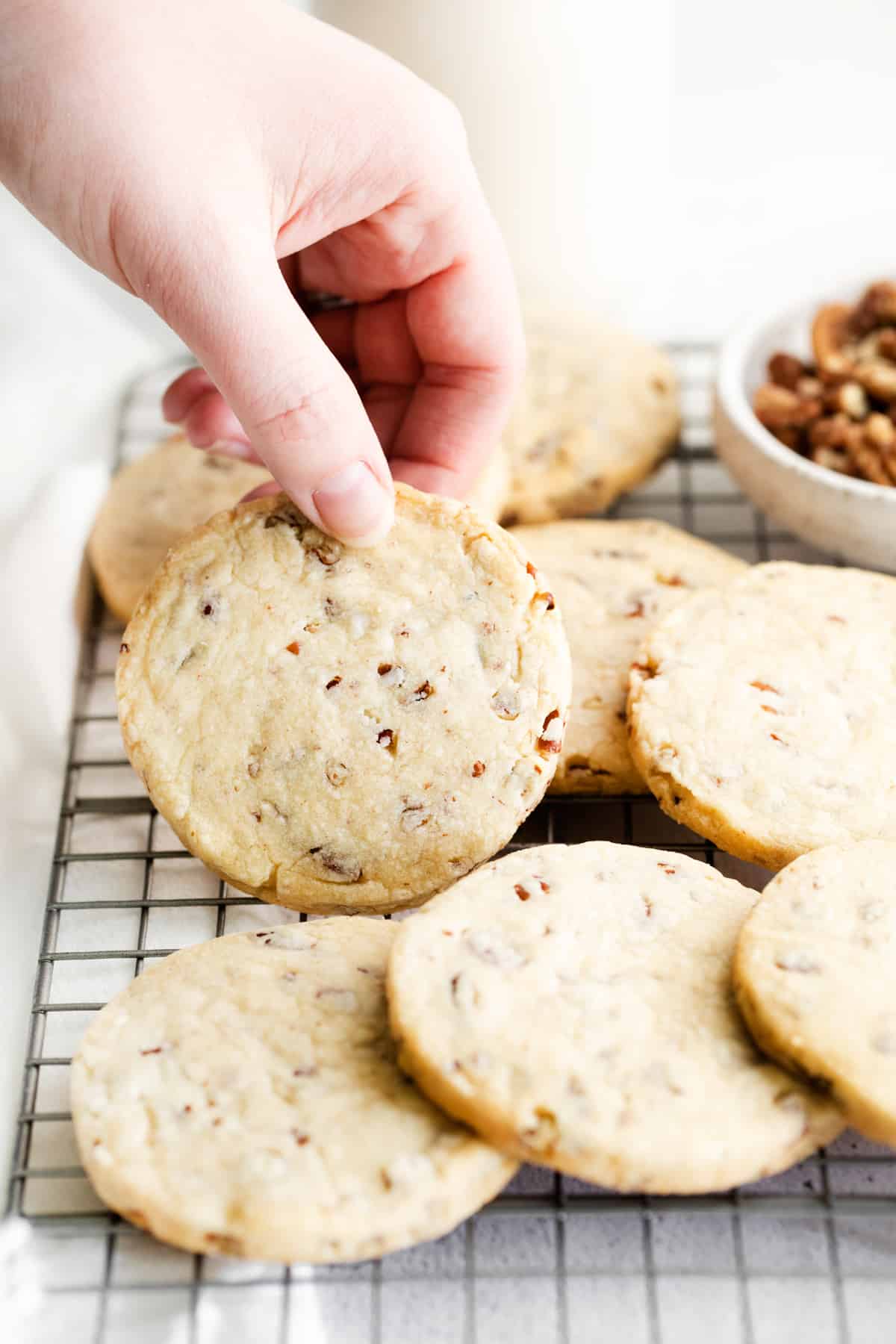 hand picking up a pecan shortbread cookie from a pile of cookies on a cooling rack