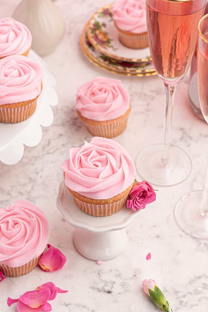 three-quarters view of a moscato cupcake on a white cupcake stand with a pink rose.