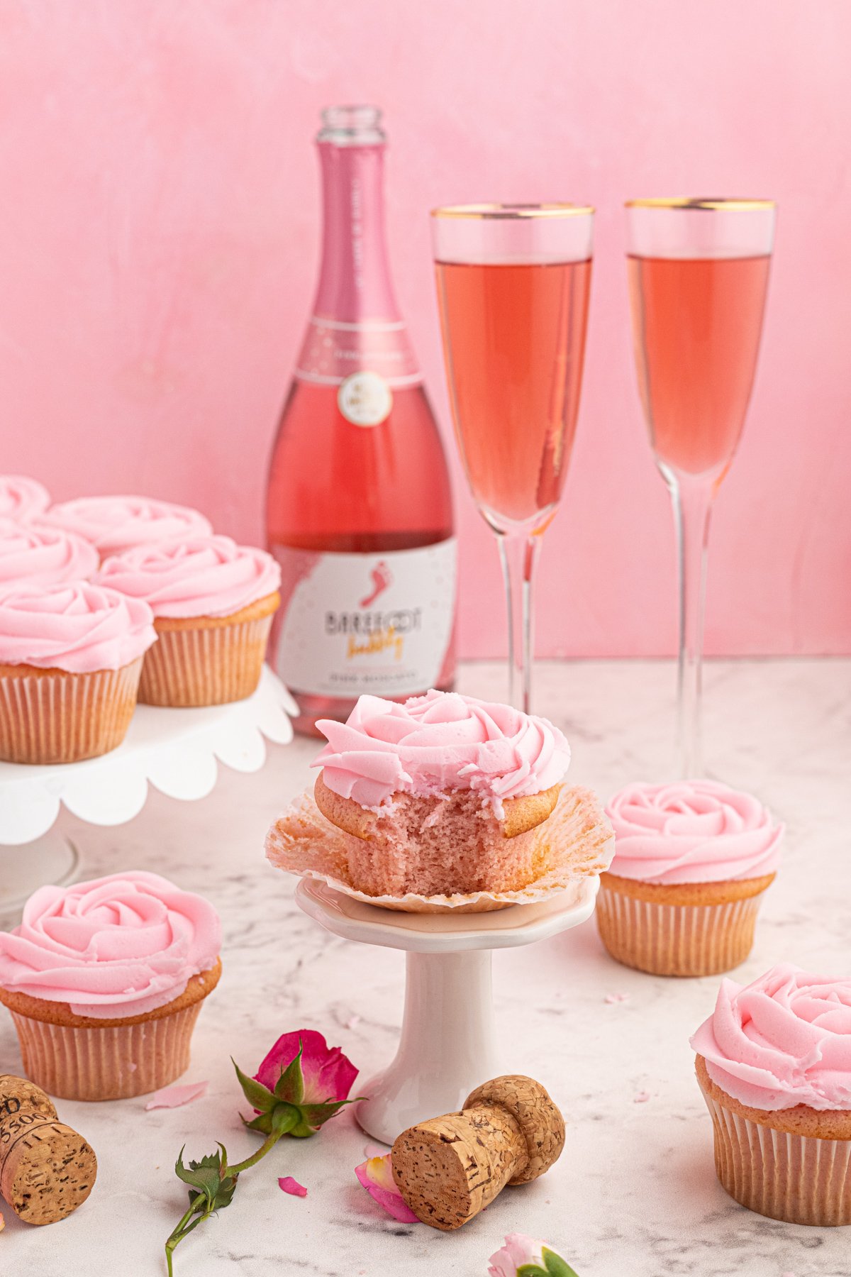 side view of a bitten moscato cupcake on a cupcake stand in front of 2 glasses of pink moscato.