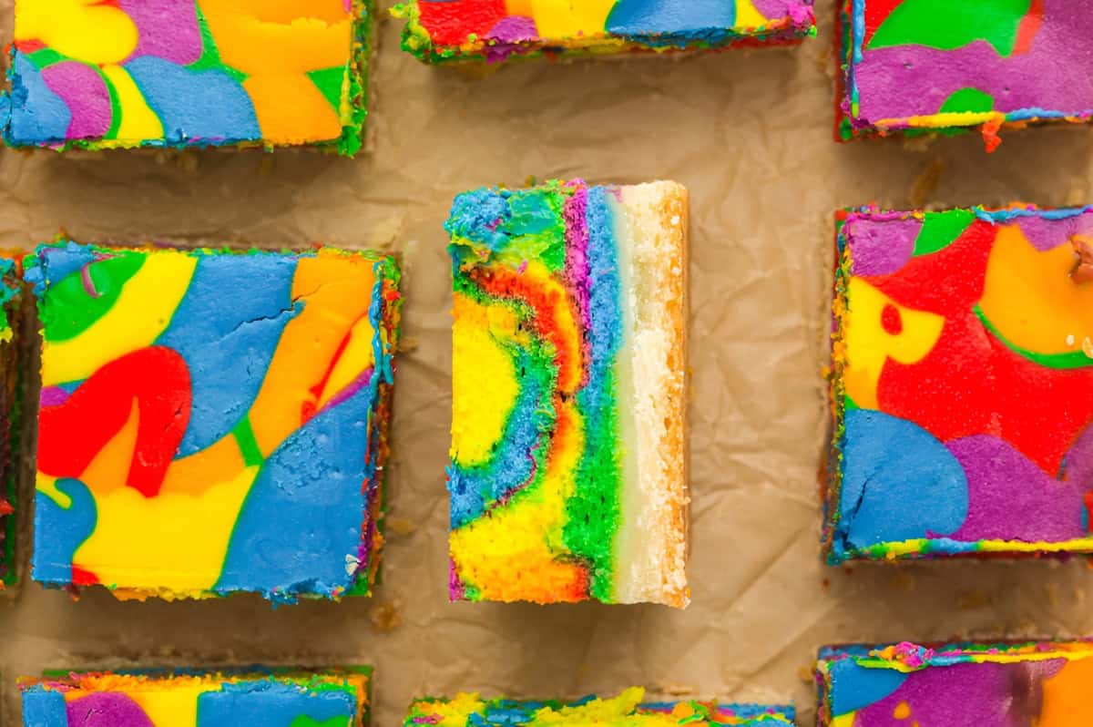 rainbow cheesecake bars on parchment, one is upturned to show the layers.