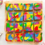 overhead view of cut rainbow cheesecake bars on parchment.