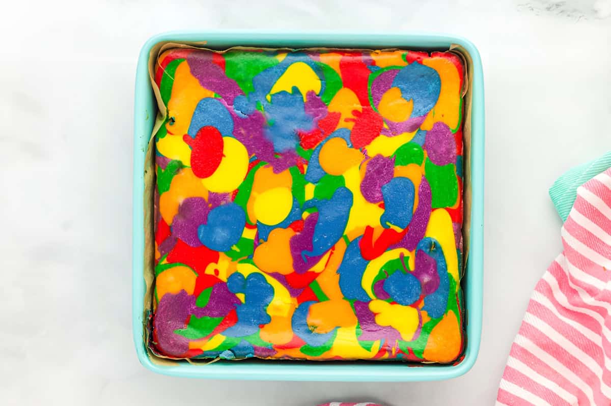 baked rainbow cheesecake in a lined square baking pan.