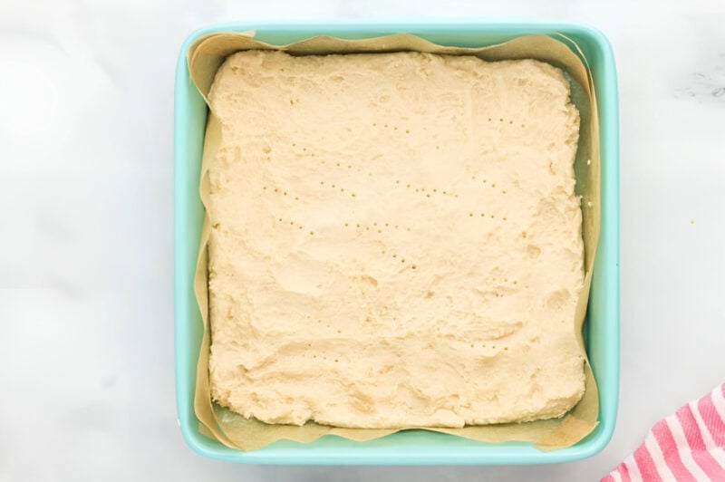 docked shortbread cookie crust in a lined square baking pan before baking.