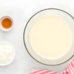 cheesecake batter in a bowl with bowls of sour cream and vanilla extract next to it.