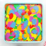 swirled rainbow cheesecake batter in a lined square baking pan.