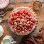 a cake with raspberries and powdered sugar on a wooden table.