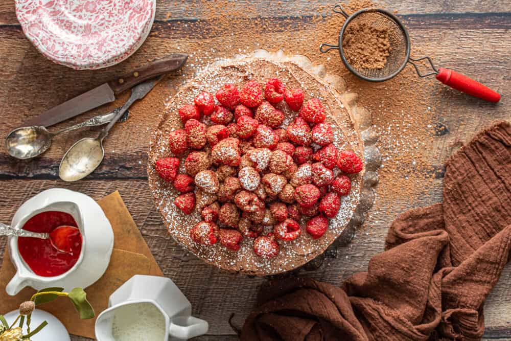 a cake with raspberries and powdered sugar on a wooden table.