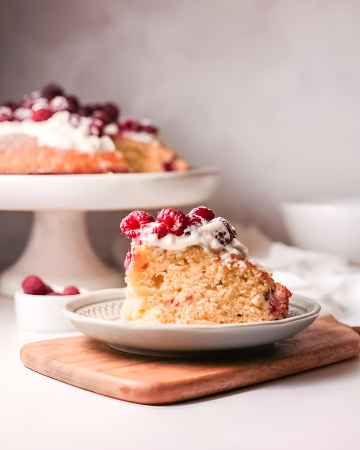 a slice of olive oil cake topped with whipped cream and fresh raspberries on a plate.