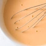 whisked eggs, olive oil, and greek yogurt in a white bowl with a whisk.