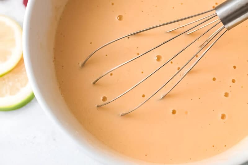 whisked eggs, olive oil, and greek yogurt in a white bowl with a whisk.