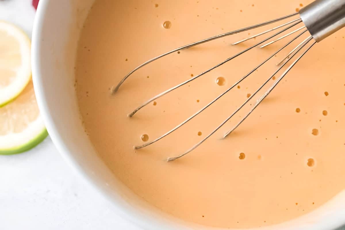 whisked eggs, olive oil, and greek yogurt in a white bowl with a whisk.
