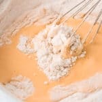 whisking wet and dry ingredients for olive oil cake in a white bowl.