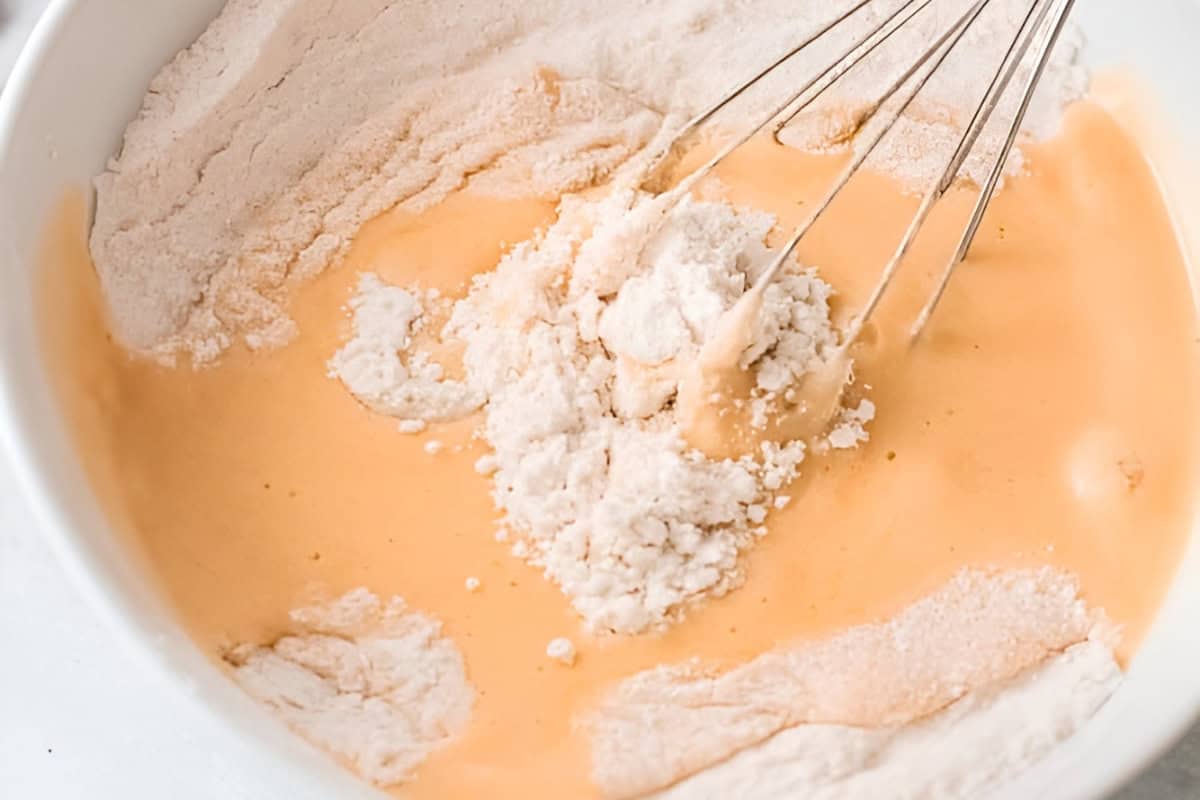 whisking wet and dry ingredients for olive oil cake in a white bowl.
