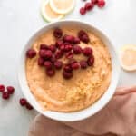 adding lemon zest and raspberries to olive oil cake batter in a white bowl.