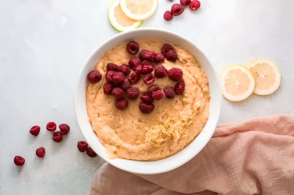 adding lemon zest and raspberries to olive oil cake batter in a white bowl.