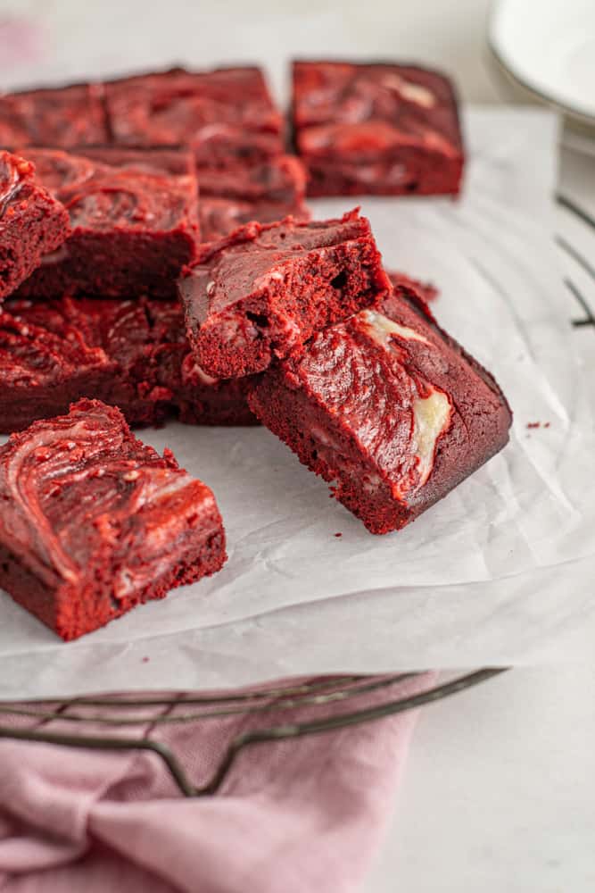 three-quarters view of red velvet cheesecake brownies on parchment, one bitten brownie is leaning up against the rest.