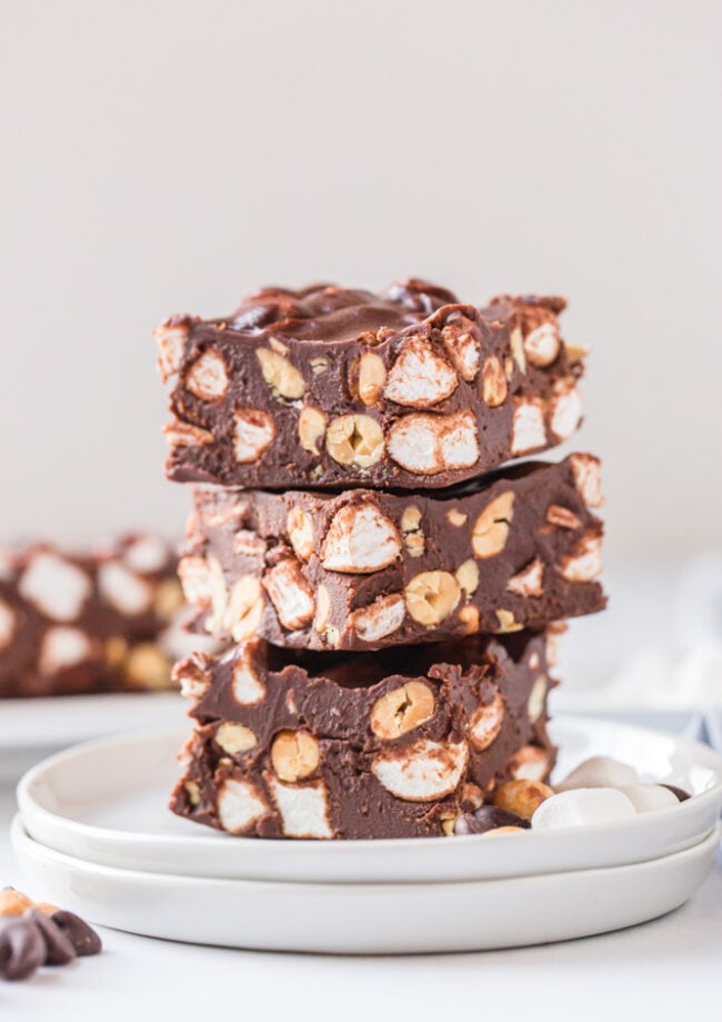 side view of 3 slices of rocky road stacked on top of each other on a white plate.