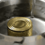 pouring water over a can of sweetened condensed milk in a large pot.