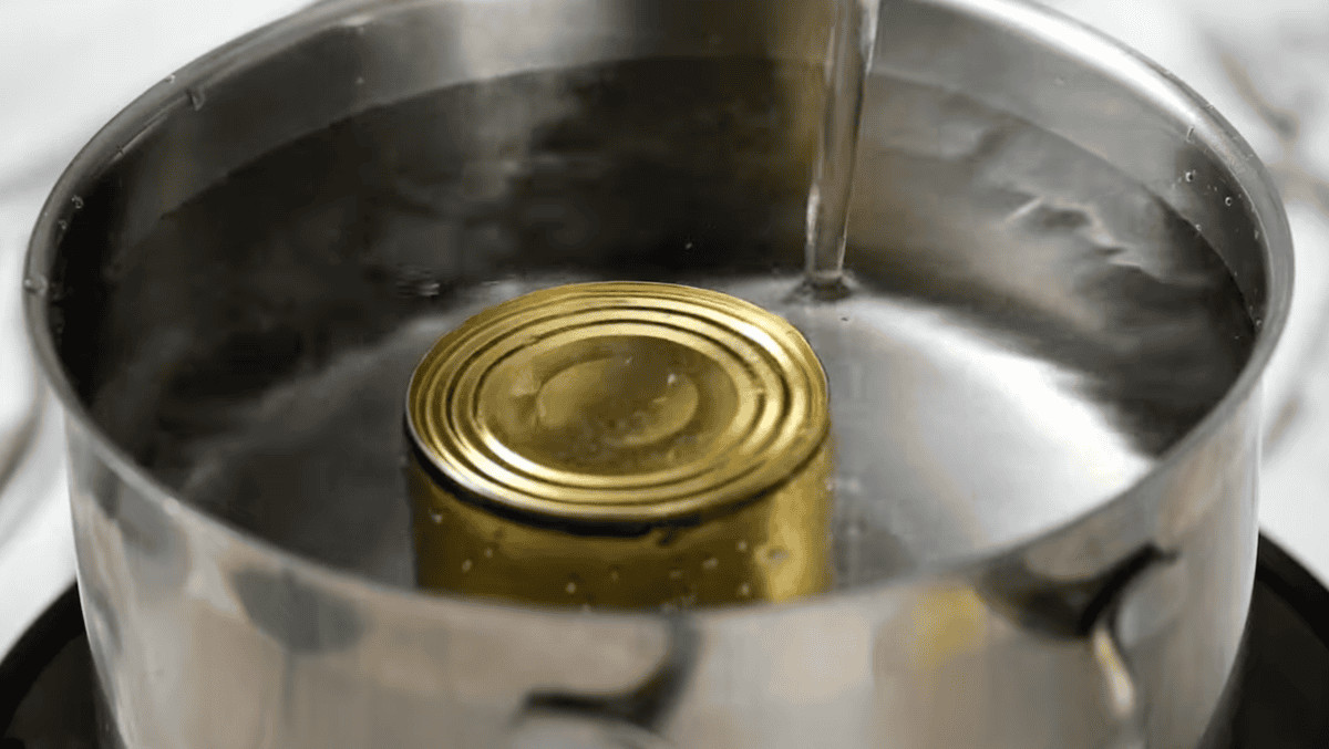 pouring water over a can of sweetened condensed milk in a large pot.