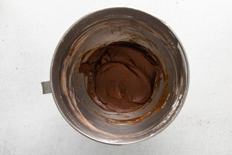 powdered sugar and cocoa added to no bake chocolate cheesecake batter in a stainless mixing bowl.