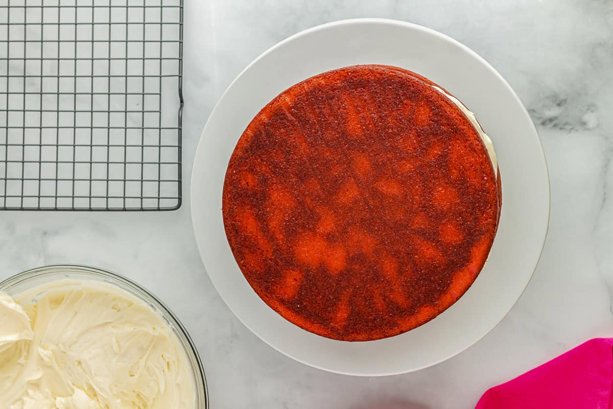 2 stacked layers of cake with frosting between them on a white cake stand.