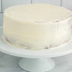 side view of a crumb-coated pink velvet cake on a white cake stand.