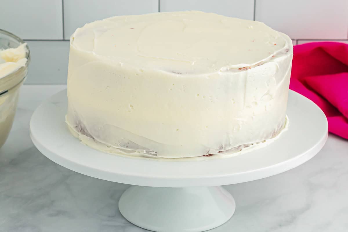 side view of a crumb-coated cake on a white cake stand.