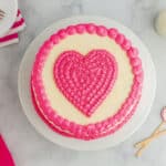 overhead view of a pink velvet cake with a pink frosted heart on top.