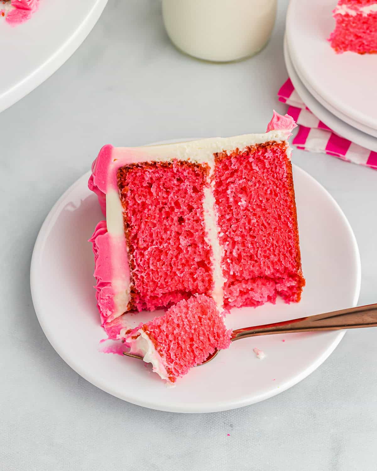 a partially eaten slice of pink velvet cake on a white plate with a fork.