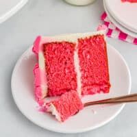 a partially eaten slice of pink velvet cake on a white plate with a fork.