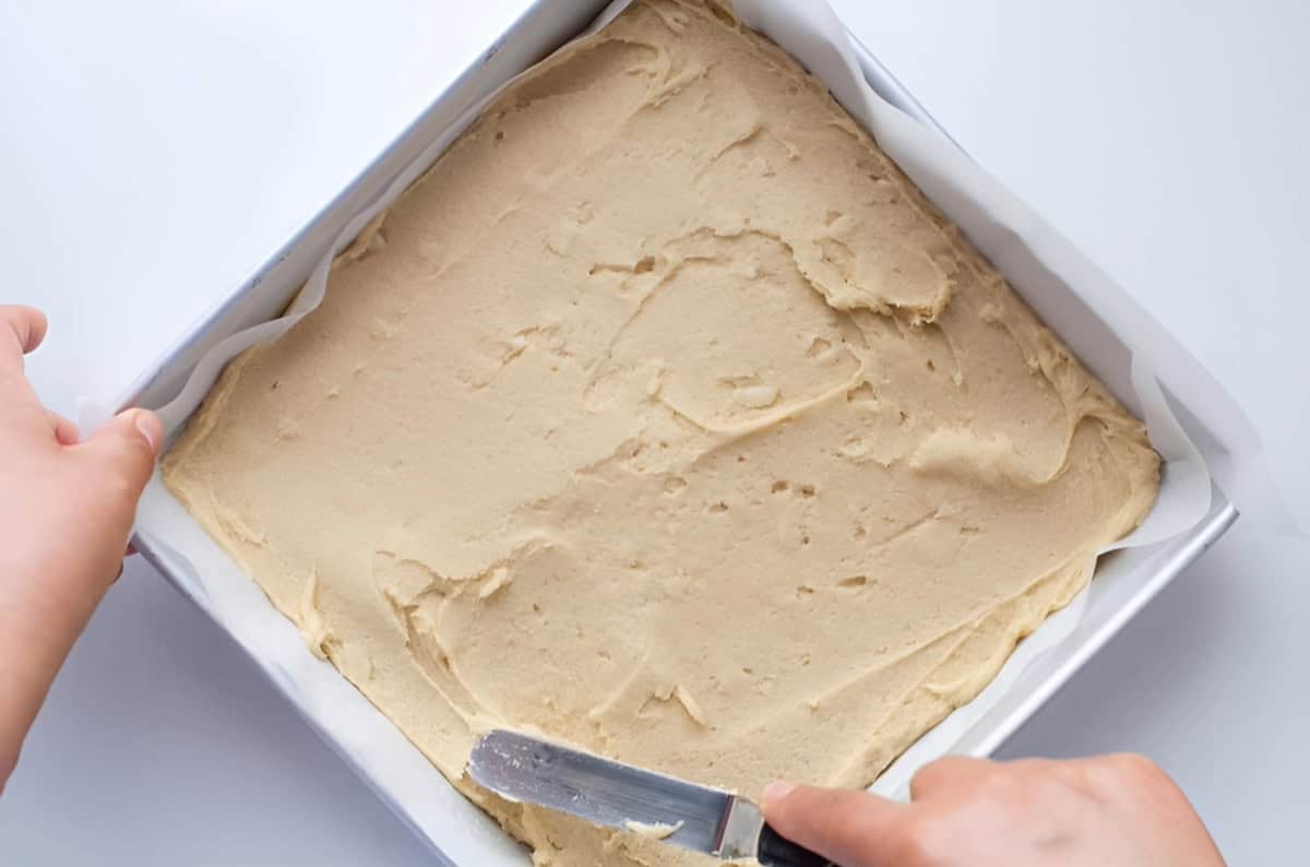 spreading blondie dough in a square baking pan with an offset spatula.
