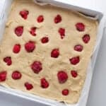 frozen raspberries atop almond blondie batter in a square baking pan.