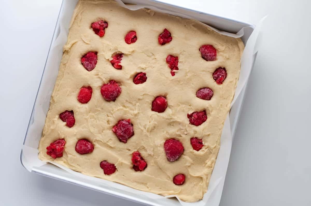 frozen raspberries atop almond blondie batter in a square baking pan.